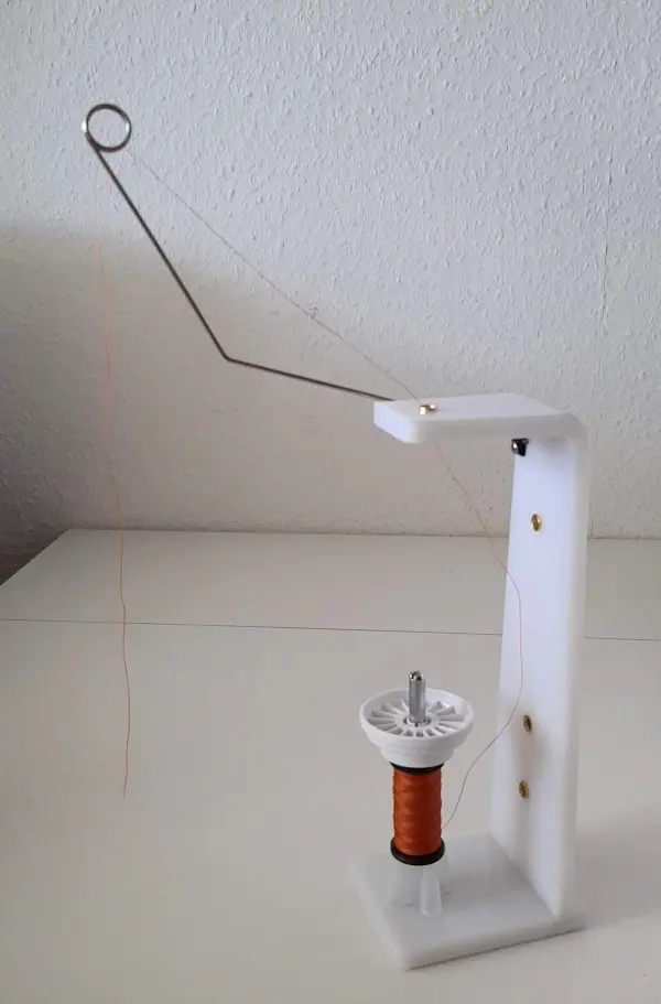Eine Spule ruht auf einem weißen Sockel, während ein Faden durch einen Bogen gespannt ist, bereit zum Nähen von Sonnenschutz.