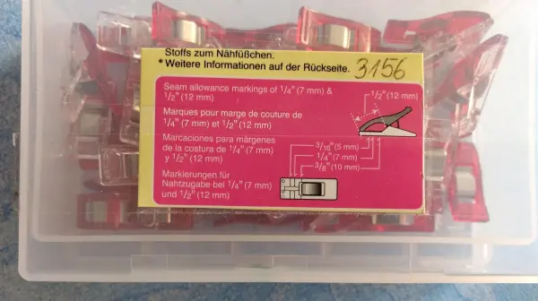 Eine transparente Box enthält mehrere rote Nähklammern, die ordentlich sortiert sind und auf einem Tisch liegen.