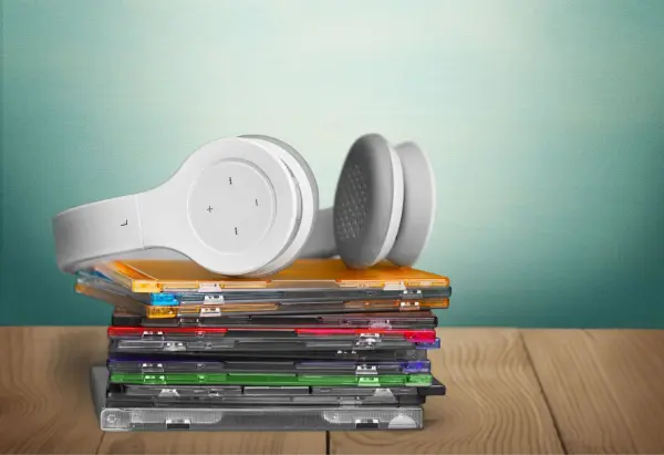 Kopfhörer liegen auf einem Stapel bunter CDs, die auf einem Holztisch platziert sind, mit einem sanften Hintergrund.