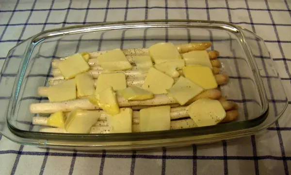 Zarte Spargelstangen liegen in einer Glasauflaufform, bedeckt mit Käse, bereit zum Backen im Ofen.