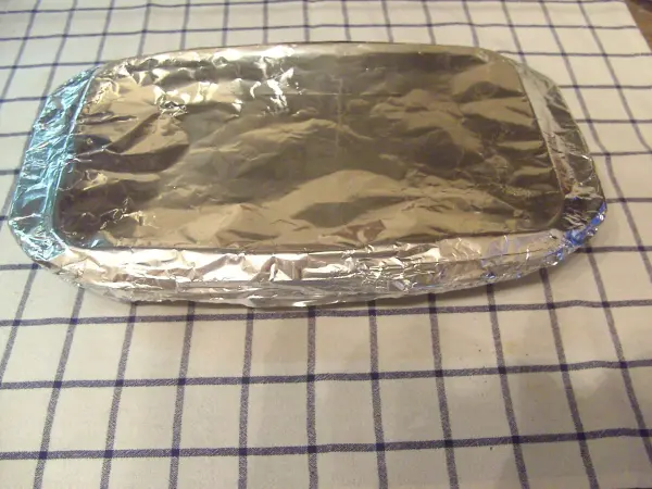 Ein mit Alufolie bedecktes Backblech steht auf einem karierten Tuch. Es bereitet leckeren Spargel aus dem Backofen vor.