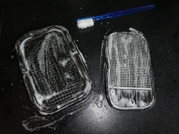 Zwei selbsthaftende Antirutschmatten liegen schaumig auf einem Tisch, während eine Bürste daneben zum Reinigen bereitsteht.