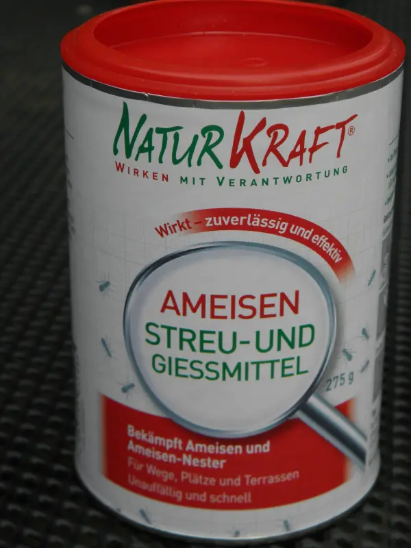 Ein Behälter mit dem Aufdruck „Ameisen Streu- und Gießmittel“ steht auf einer Oberfläche, bereit zur Bekämpfung von Ameisen im Blumenkübel.