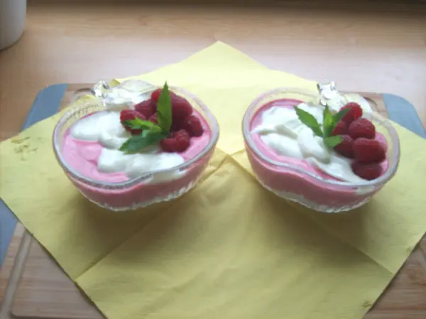 Zwei Glasschalen mit Quark-Frischkäse-Himbeer-Dessert, garniert mit Himbeeren und Minze, auf einer gelben Serviette.