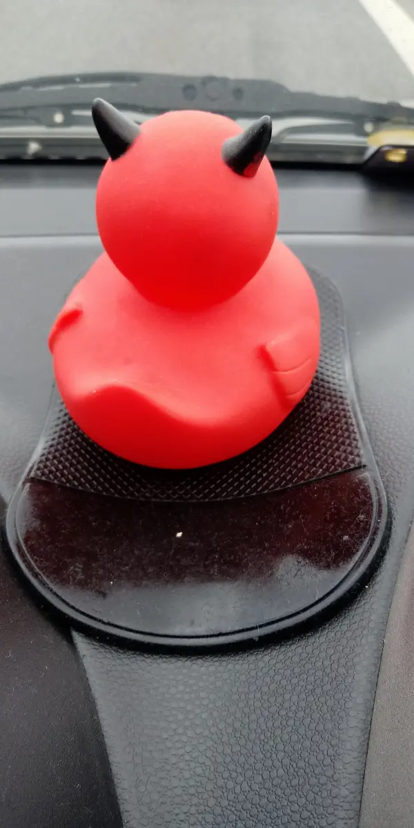 Eine rote Gummikugel mit Teufelshörnern sitzt auf einer Antirutschmatte auf dem Armaturenbrett eines Autos.