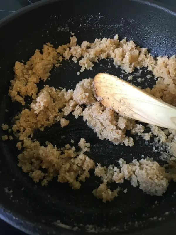 In einer Pfanne wird eine krümelige Mischung aus braunem Zucker und Butter mit einem Holzlöffel gerührt, um eine Füllung für die schwedischen Blaubeer-Tartelettes herzustellen.