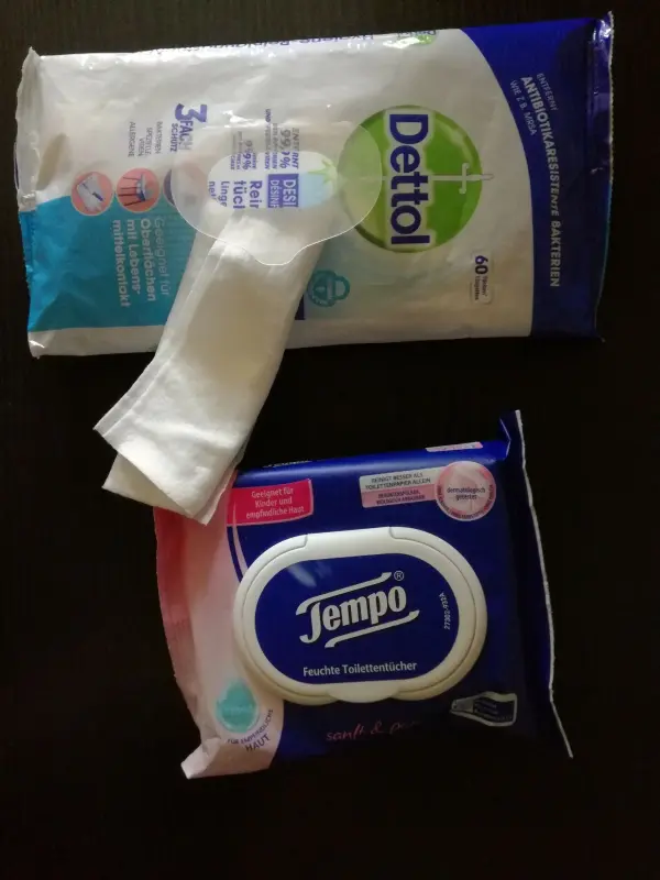 Reinigungstücher liegen auf einem Tisch. Eine Packung Dettol und eine von Tempo sind sichtbar und gut verpackt.
