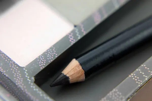 Ein schwarzer Kajalstift liegt in einem Kosmetikbehälter und zeigt die spitz zulaufende, angespitzte Mine.