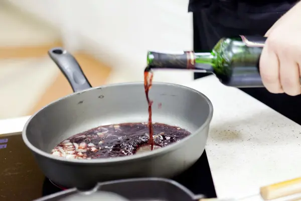 Rotwein wird in eine Pfanne gegossen, um in der Küche Soßen für besseren Geschmack zuzubereiten.