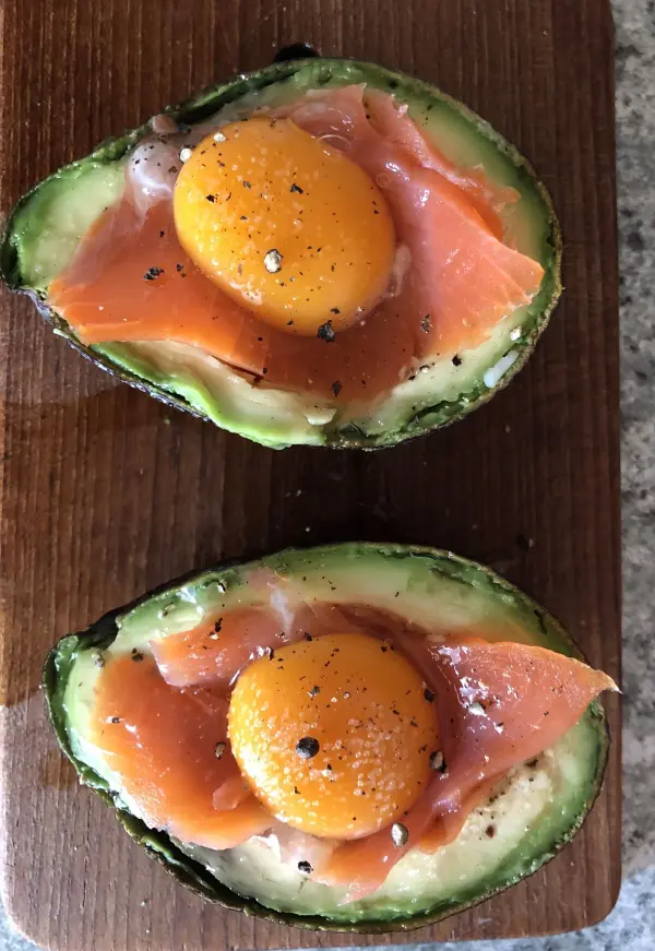 Halbierte Avocado mit Lachs und einem Eigelb, auf einem Holzbrett angerichtet, bereit zum Backen.