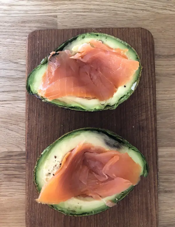 Eine halbierte Avocado liegt auf einem Holzbrett, gefüllt mit zartem Lachs, bereit zum Backen im Ofen.
