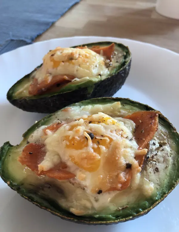 Gefüllte Avocado mit Lachs und Ei auf einem Teller, gebacken und serviert, umgeben von einem neutralen Hintergrund.
