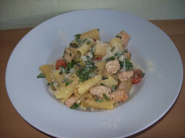 Rigatoni in einer weißen Schüssel, gemischt mit Kräutern und Sauce, serviert auf einem Holzuntergrund.