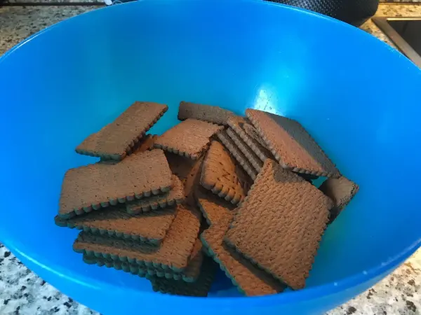In einer blauen Schüssel liegen braune Kekse, die darauf warten, für ein erfrischendes Erdbeerdessert verwendet zu werden.