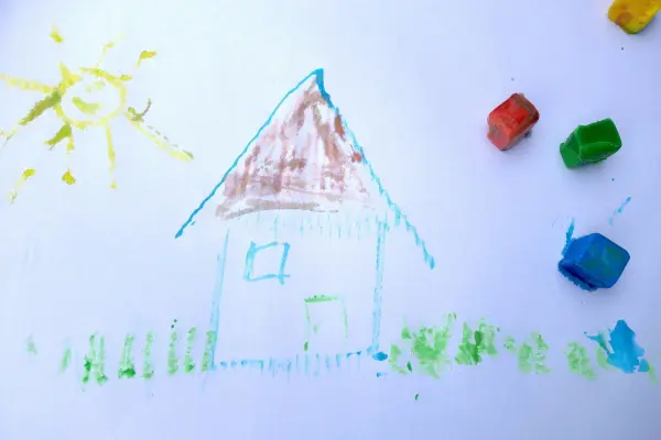 Bunte Eiskreide liegt neben einer Zeichnung eines Hauses unter der Sonne, die auf Papier entsteht.