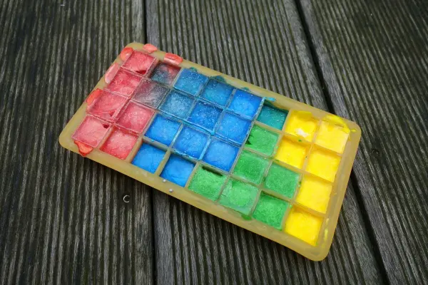 Bunte Eiskreide aus einer Form liegt auf einem Holzbrett, bereit zum Spielen und Zeichnen im Sommer.