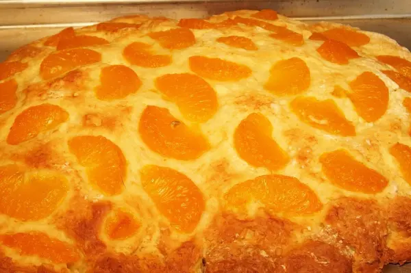 Ein Blechkuchen mit saftigen Mandarinenstücken ist goldbraun gebacken und liegt warm auf einem Blech.