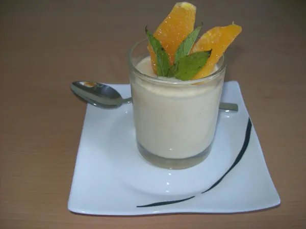 Ein Orangen-Dessert in einem Glas mit frischen Orangenscheiben und Minze, serviert auf einem weißen Teller.