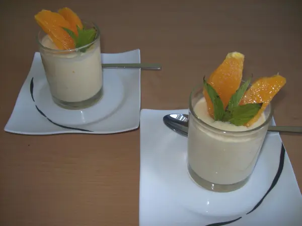 Einfache Orangen-Desserts stehen in gläsernen Schalen, dekoriert mit Orangenscheiben und Minzblättern, auf weißen Tellern.