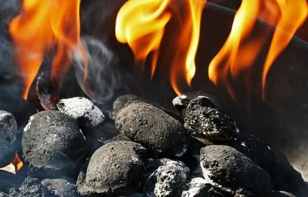 Schwarze Grillkohlen brennen, während Flammen aufsteigen, und zeigen eine alternative Methode, um Nachos anzuzünden.