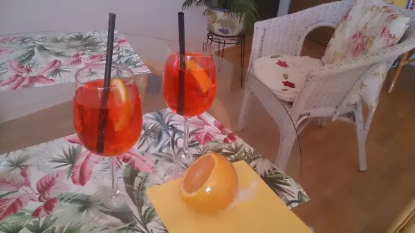 Zwei Cocktails mit Orangenscheiben stehen auf einem bunten Tisch, neben einer angeschnittenen Orange in einem einladenden Raum.