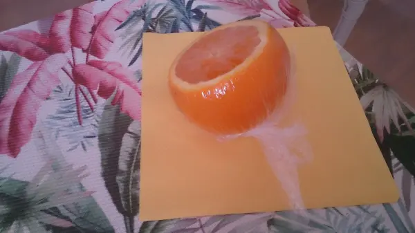 Eine angeschnittene Orange liegt auf einem gelben Teller, während Saft herunterläuft; der Hintergrund zeigt ein blattartiges Muster.