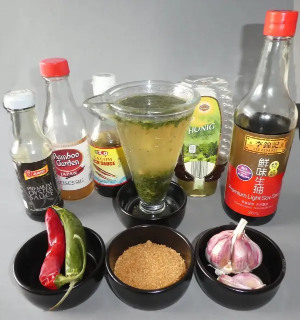 Ein Glas scharfe Knoblauchsoße steht in der Mitte, umgeben von Zutaten wie Chili, Knoblauch und verschiedenen Saucen.