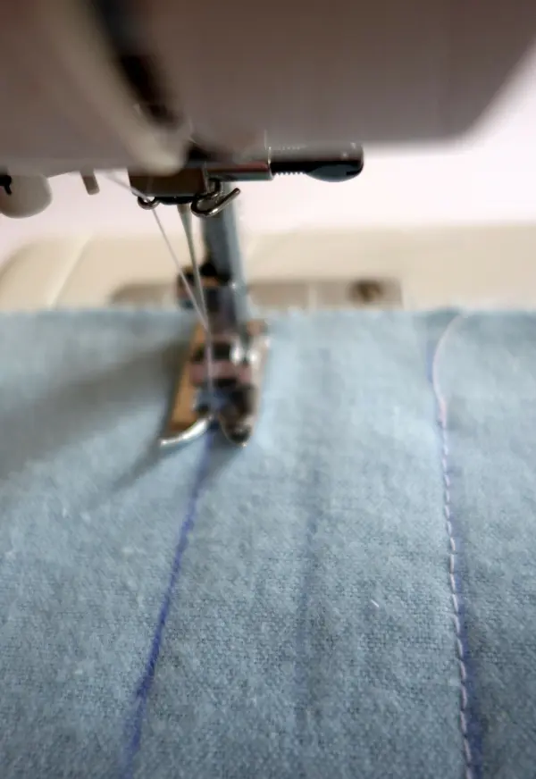 Eine Nähmaschine bearbeitet einen blauen Stoff, während ein Staubwedel als DIY-Projekt in der Umgebung vorbereitet wird.