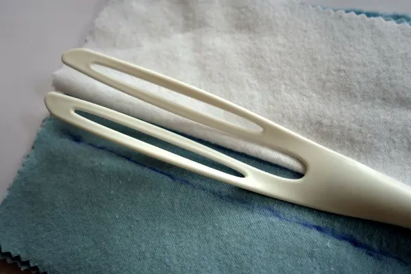 Ein weißer, länglicher Staubwedel liegt auf einem blauen Tuch, bereit zum Staubwischen in einem sauberen Raum.