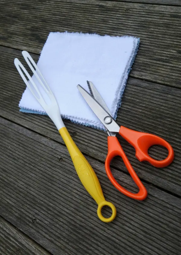 Ein wiederverwendbarer Staubwedel wird aus einem weißen Stofftuch, einer gelben Gabel und einer orangefarbenen Schere zusammengestellt.