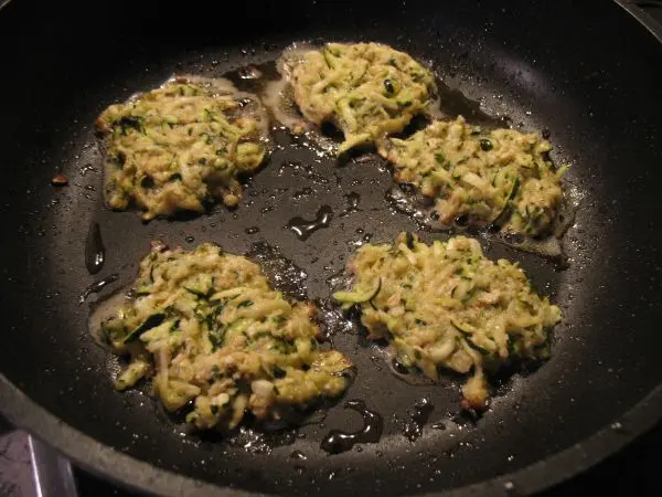Knusprige Zucchini-Rösti braten in einer Pfanne mit Öl, während sie goldbraun werden und leicht sprudeln.