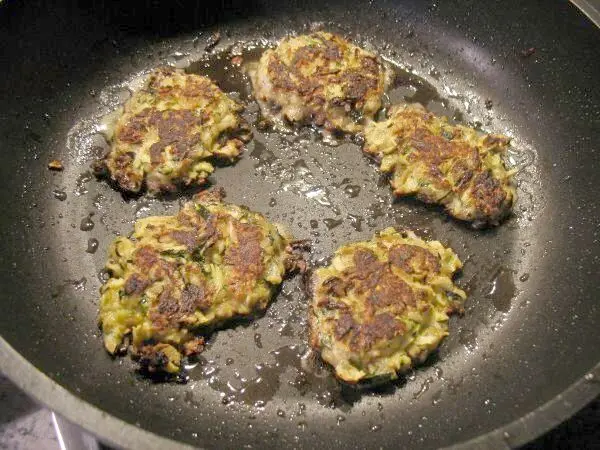 Knusprige Zucchini-Rösti braten in einer Pfanne, umgeben von köstlichem, goldbraunem Käse und Zucchini.