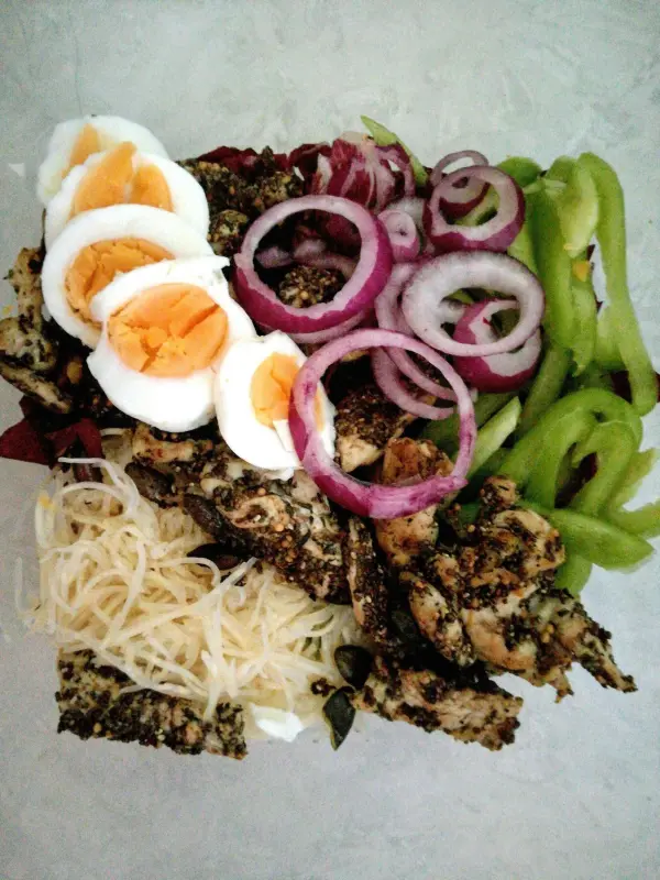 Ein bunter Salat aus Radicchio und Paprika mit Putenstreifen, hartgekochten Eiern und frischem Gemüse auf einem Teller.