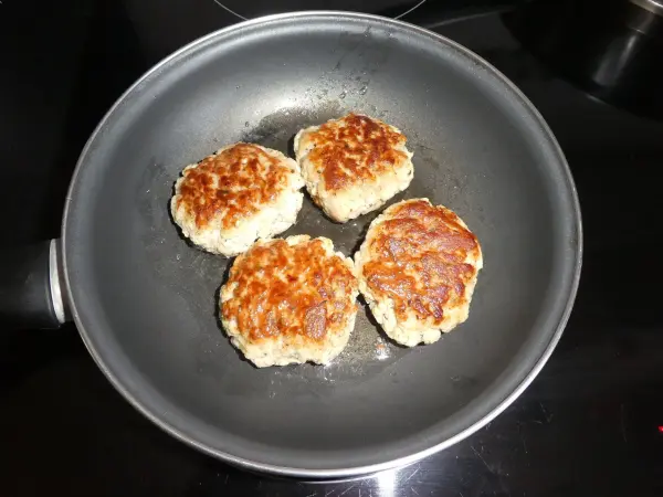 Käse-Frikadellen braten in einer Pfanne, umgeben von einer glänzenden Oberfläche, bereit für ein leckeres Gericht.