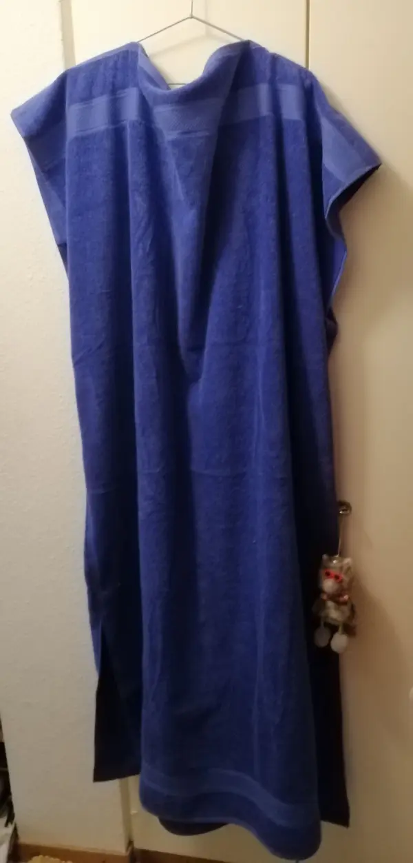 Ein blaues Badeüberziehkleid aus Duschtüchern hängt an einer Wand und zeigt die einfache, praktische Form.