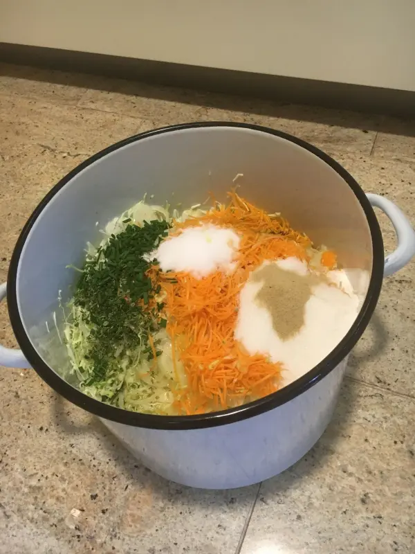 Eine große Schüssel enthält frischen Krautsalat mit gehobeltem Gemüse, Zucker und Gewürzen, bereit zum Mischen.