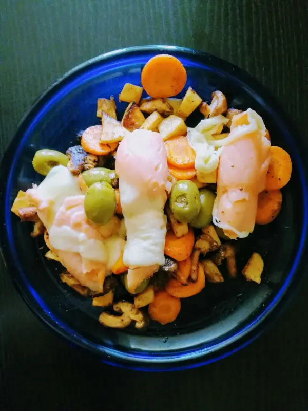 Auf einem blauen Teller liegen bunte Gemüsestücke wie Karotten und Oliven, garniert mit Lachs-Käse-Röllchen.