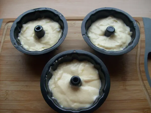 Drei runde Silikonformen mit einer cremigen Grießmasse stehen auf einem Holzbrett, bereit zum Backen.