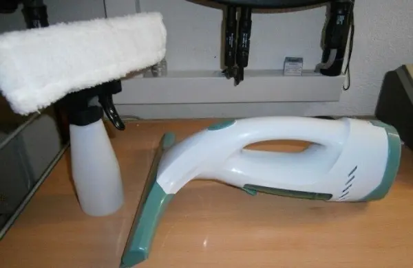 Ein Akku-Fensterreiniger liegt neben einem Sprühbehälter auf einem Tisch, bereit für die Reinigung von Fenstern.