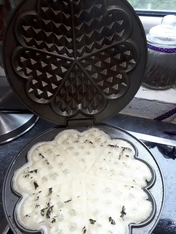 Ein Waffeleisen mit angebackenem Teig steht geöffnet auf einer Arbeitsfläche, bereit zur Reinigung mit Speisestärke.