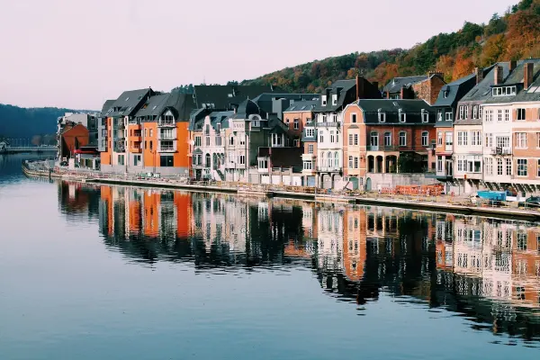 Bunte Häuser spiegeln sich im ruhigen Wasser eines Flusses, umgeben von sanften Hügeln und klarer Abenddämmerung.