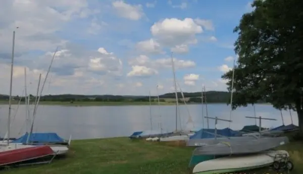 Segelboote liegen friedlich am Ufer eines Gewässers, umgeben von einer ruhigen Landschaft und wolkenverhangenem Himmel.