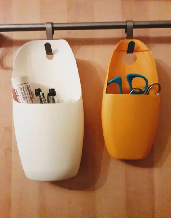 Zwei DIY-Halterungen für Kunststoffdeckel hängen an einer Stange, gefüllt mit Schreibutensilien und Scheren.