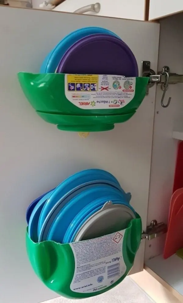 Ein grüner DIY-Halter für Kunststoffdeckel hängt unter einem Küchenschrank und fasst mehrere farbige Deckel.