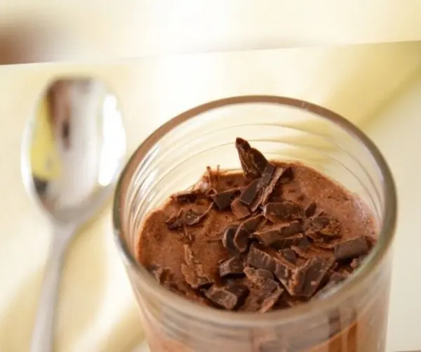 Eine Schüssel Mousse au Chocolat wird appetitlich präsentiert, garniert mit Schokoladenstückchen, auf einem hellen Hintergrund.