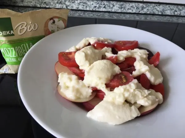 Ein Teller mit Nektarinen und Tomatensalat, garniert mit Mozzarella, auf einer Küchenoberfläche.