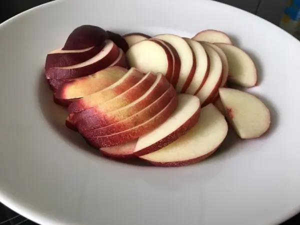 In einer weißen Schüssel liegen frisch geschnittene, saftige Nektarinen-Scheiben, bereit für einen erfrischenden Salat.