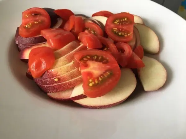 Nektarinen- und Tomatenscheiben sind frisch auf einem weißen Teller angerichtet, bereit zum Servieren in einem hellen Küchenumfeld.