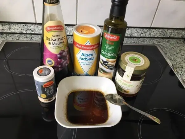 Eine Schüssel mit einer dunklen Marinade steht auf einem Tisch, umgeben von verschiedenen Flaschen und Gewürzen für den Nektarinen-Tomatensalat.