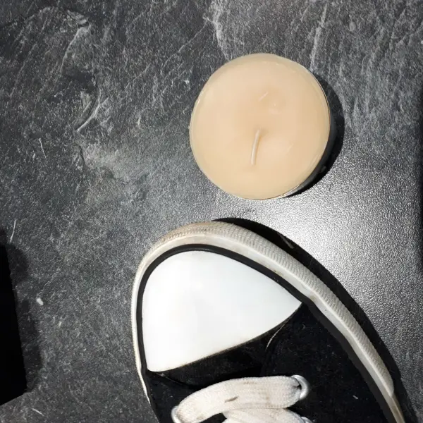 Die Turnschuhe mit weißen Kappen stehen auf einem dunklen Untergrund neben einer schützenden Creme, die sie vor Schmutz bewahrt.